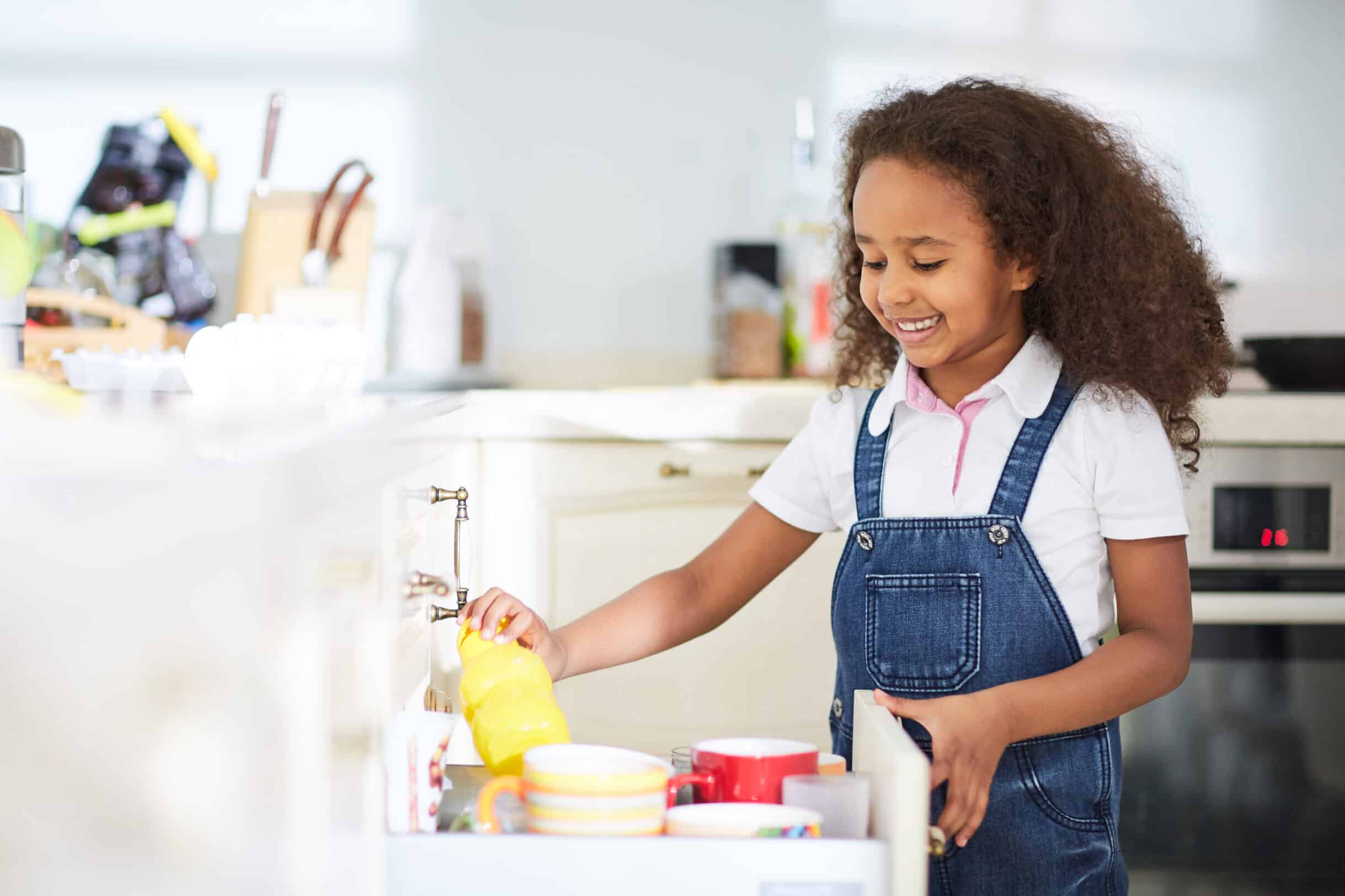 Little girl choosing mug in kitchen drawer